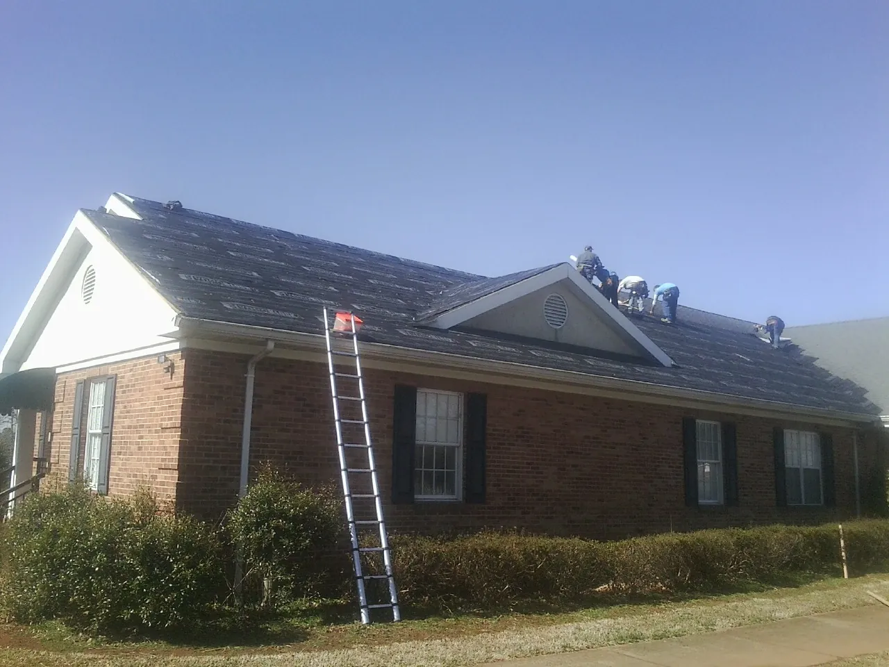 Crew tearing shingles off a brick ranch roof with a ladder set — Emergency Roof Repair work by our crew in Plainfield