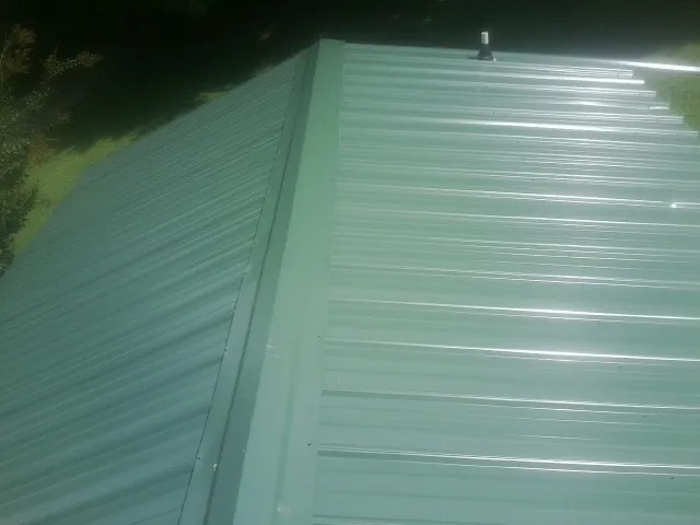New green metal panels meeting at the ridge of a roof — Flat Roof Repair work by our crew in Plainfield